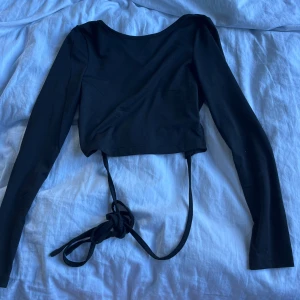 Svart croppad topp med knytband - Snygg svart croppad topp med långa ärmar och knytband i midjan som kan knytas både fram och bak. Aldrig använd 