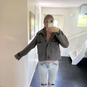 Grå kavajjacka med stora fickor - Säljer en grå  kavajjacka med stora framfickor och bred krage. Jackan har knappar framtill och en rak, boxig passform. Perfekt för dig som gillar en trendig och stilren look.