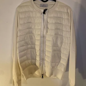 Vit quiltad cardigan jacka från Moncler - Säljer en stilren vit cardigan jacka från Moncler med quiltade paneler framtill och ribbade muddar. Jackan har dragkedja och rund halsringning. Perfekt för dig som vill ha en lätt och snygg jacka, kvitto och påse finns.