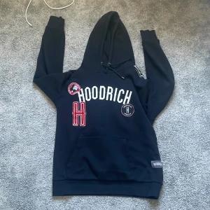 Svart hoodie från Hoodrich - Säljer en svart hoodie från Hoodrich i storlek L. Tröjan har stora vita och röda tryck och broderade märken framtill. Mjuk bomullskänsla.  Pris kan diskuteras vid snabb affär!