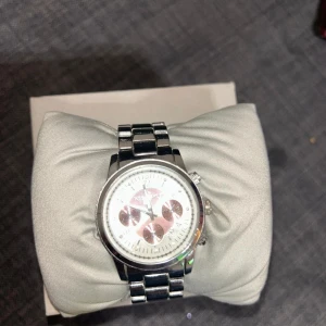 Silverfärgad klocka från Michael Kors - Snygg klocka från Michael Kors i silverfärgat rostfritt stål. Klockan har en rund urtavla med tre mindre urtavlor och romerska siffror. Länken är robust och klassisk, perfekt för dig som gillar stilrena accessoarer.... det är original klocka men kartongen finns inte kvar tyvärr.