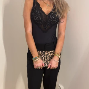Svart spetsbody med v-ringning - Säljer en svart body med v-ringning och spetsdetaljer upptill. Bodyn har smala axelband och är figurnära, perfekt att styla till både jeans och kjol. Spetsen ger en elegant touch och materialet känns mjukt mot huden.