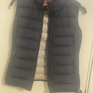 Parajumper väst - Snygg mörkblå dunväst från Parajumpers med dragkedja framtill och två sidofickor. Västen har quiltad design och ljusgrå insida. Perfekt för lager-på-lager och enkel att matcha med olika outfits. Storlek S super lightweight.