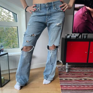 Ljusblå slitna jeans från Levi's - Ljusblå jeans från Levi's med raka ben och flera slitningar och hål på framsidan. Klassisk femficksmodell med knappgylf och normal passform. Perfekta för en avslappnad och trendig look. de är utsydda