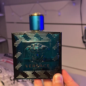 Versace Eros herrparfym - Versace Eros herrparfym i en stilren, fyrkantig flaska i turkost glas med guldblått lock och Medusa-detalj. Flaskan har tydliga Versace-mönster och logga framtill. En ikonisk doft för dig som gillar lyxiga och fräscha parfymer den har ungefär 40ml kvar i flaskan 