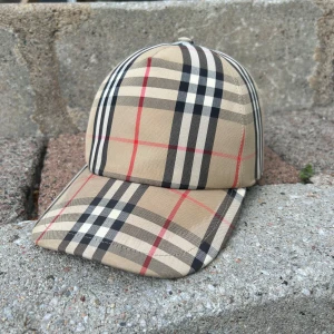 Beige rutig keps från Burberry - Säljer en klassisk beige rutig keps från Burberry i storlek M. Kepsen har det ikoniska rutmönstret i beige, svart, vitt och rött. Tillverkad i bomull och polyester, perfekt för en stilren look. Köpt på Mytheresa och kvitto finns! Inga direkta defekter. Om det är något mer du undrar är det bara att skriva😃