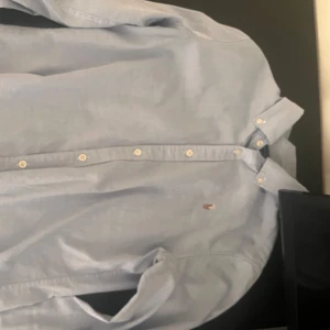Ljusblå skjorta från Ralph Lauren - Klassisk ljusblå skjorta från Ralph Lauren med knappar framtill och broderad logga på bröstet. Skjortan har lång ärm och en stilren, tidlös design som passar till många tillfällen. Är i strlk 16 år men skulle säga att om man är 160 typ så passar den bra pris kan diskuteras
