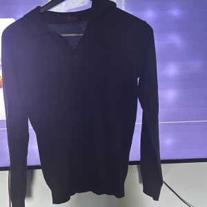 Svart pikétröja från Indicode - Säljer en svart långärmad pikétröja från Indicode i storlek XS. Tröjan har klassisk krage och knäppning framtill. Perfekt för en stilren och enkel look.