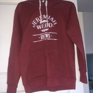 Vinröd hoodie med tryck 'Jeremiah Weed Brews' - Säljer en vinröd hoodie från Jeremiah Weed med vitt tryck framtill. Tröjan har huva med vita snören och en stor magficka. Skriv vid frågor och funderingar!!!❤️
