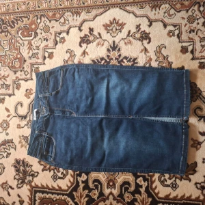 Mörkblå jeanskjol - Säljer en klassisk mörkblå jeanskjol med raka linjer och femficksdesign. Kjolen har normal passform och är tillverkad i denim. Perfekt att styla med en enkel topp eller hoodie.