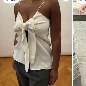 Vit linnetopp med stor rosett - Säljer en vit linnetopp från djerf avenue med smala axelband och en stor rosett framtill. Toppen har en elegant v-ringning och är tillverkad i ett lätt, glansigt material som ger en lyxig känsla. Storlek S