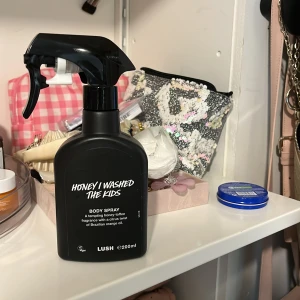 Honey I Washed The Kids Body Spray från Lush - En svart sprayflaska med body spray från Lush, doften heter Honey I Washed The Kids. Flaskan rymmer 200 ml och har en enkel, modern design med vit text. Produkten ger en söt och varm doft av honung och karamell. helt ny oanvänd 
