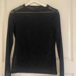 Svart meshtröja från Vero Moda - Säljer en svart långärmad meshtröja från Vero Moda. Tröjan är genomskinlig och har en tight passform, perfekt att styla i lager på lager. Enkel och stilren design med rund halsringning.