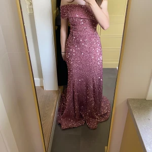 Rosa glittrig långklänning med paljetter - Säljer en fantastisk rosa långklänning täckt av glittrande paljetter. Klänningen har offshoulder-modell och figurnära passform upptill som sedan faller ut i en elegant kjol. Perfekt för bal eller fest!