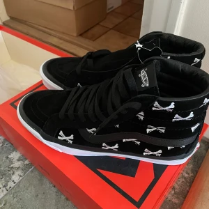 Svarta Vans Sk8-Hi WTAPS med broderade korslagda ben us9 - Säljer ett par svarta Vans Sk8-Hi i samarbete med WTAPS. Skorna har broderade vita korslagda ben över hela ovandelen och klassisk vit sula. Perfekta för dig som gillar unika sneakers med coola detaljer. Us9