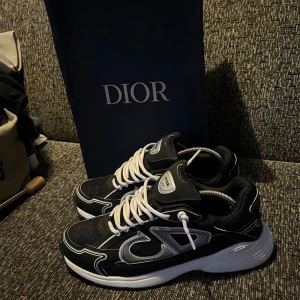  Dior B30 - Säljer ett par svarta Dior sneakers med vita detaljer och snörning. Skorna har en sportig design med rund tå, platt sula och tydliga kontrastsömmar. Perfekta för dig som gillar exklusiva och trendiga sneakers.