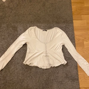 Vit croppad bolerotopp med spets från Gina tricot - Säljer en söt vit croppad bolerotopp från Gina tricot. Toppen har långa ärmar, spetsdetaljer längs kanterna och en liten rosett framtill. Perfekt för lager-på-lager och ger en romantisk touch till outfiten.