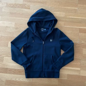 Svart zip hoodie från Polo Ralph Lauren - Säljer en zip hoodie från Polo Ralph Lauren. Tröjan har huva med snörning och två fickor framtill. Hoddien har nästan aldrig blivit använd. Ny pris ligger på 2300kr. Pris kan diskuteras vid snabb affär. 