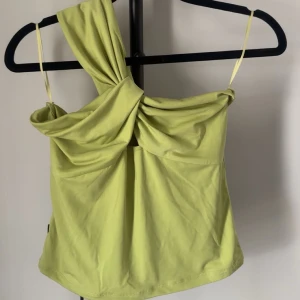 Ljusgrön one shoulder topp - Trendig ljusgrön topp med one shoulder-design och twistad detalj framtill. Tunt och mjukt material med smala axelband på ena sidan. Perfekt för sommarens alla tillfällen. Lappen kvar!