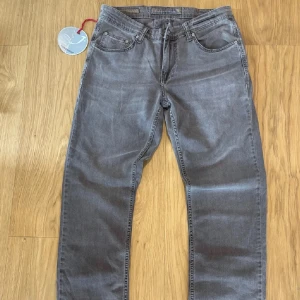 Grå jeansbyxor från Replay - Säljer ett par grå jeansbyxor från Replay med klassisk femficksdesign och raka ben. Byxorna har normal passform och tydliga Replay-detaljer på bakfickan. Perfekta för dig som gillar stilrena och tidlösa jeans.