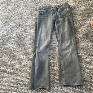 Grå jeansbyxor med broderade bakfickor från Gina Tricot - Säljer ett par grå jeansbyxor från Gina Tricot med snygga broderade detaljer på bakfickorna. Byxorna har klassisk femficksdesign och med  utsvängd bootcut-stil. Perfekta för dig som vill ha något unikt i garderoben!