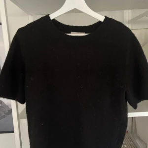 Svart stickad kortärmad tröja från H&M - En svart stickad tröja från H&M med korta ärmar och rund halsringning. Tröjan har en enkel och stilren design, perfekt att matcha med olika outfits. Mjuk och bekväm känsla tack vare det stickade materialet.