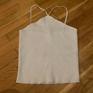 Vit ribbad linnetopp från Zara - Säljer en vit ribbad linnetopp från Zara med tunna axelband. Toppen har en enkel och stilren design, perfekt för varma dagar eller som layering-plagg. Materialet är mjukt och stretchigt för en bekväm passform.