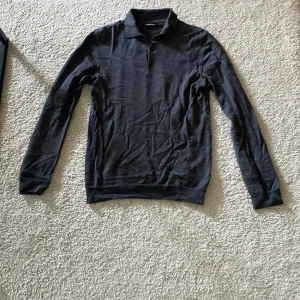 Mörkgrå pikétröja från J.Lindeberg - Säljer en stilren mörkgrå pikétröja från J.Lindeberg. Tröjan har klassisk krage, knäppning med tre knappar och diskret logga på bröstet. Perfekt för en clean och avslappnad look.