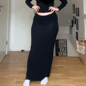 Svart långkjol med stretch - Svart maxikjol med figurnära passform. Kjolen är enkel i designen utan synliga detaljer och har en mjuk, stretchig känsla. Perfekt för dig som gillar minimalistisk stil. Aldrig använd. Storlek M