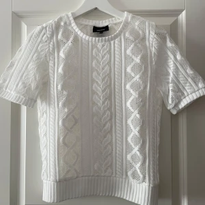 Vit topp - Säljer en vit topp från Object med korta ärmar och snyggt mönster. Tröjan har rund halsringning och ribbade kanter. Perfekt för lager-på-lager eller sommarens svalare dagar.