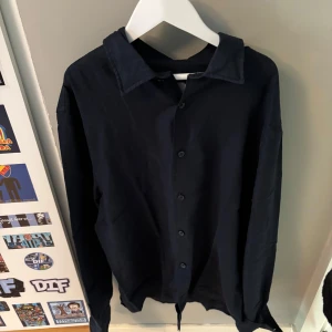 Svart långärmad skjorta i bomull - Stilren svart skjorta från dressman med klassisk krage och knäppning framtill. Skjortan är långärmad och har en rak, något loose passform. Perfekt att styla med jeans eller dressade byxor för en clean look.