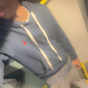 Mörkblå hoodie från Polo Ralph Lauren - Snygg mörkblå hoodie från Polo Ralph Lauren med vit snörning och klassisk röd logga på bröstet. Tröjan har huva, känguruficka och långa ärmar. Perfekt för en chill och stilren look.