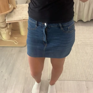 Blå jeanskjol från gina  - Säljer en klassisk marinblå jeanskjol från gina, modell Molly. Kjolen är kort, har fem fickor och stängs med dragkedja och knapp framtill. Perfekt passform och snygg till sneakers eller boots. Enkel och tidlös stil som funkar året runt.