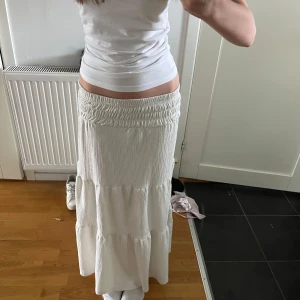 Vit långkjol med volanger - Supersöt low-waist vit långkjol. Andvänd några fåtal gånger! Har en liten defekt vid slutet av kjolen men går säkert bort i tvätten. Har super många kjolar då den här inte kommer till andvändning. Men är super fin och finns ej att få tag på längre💕