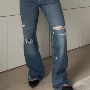 Blå slitna wide jeans - Säljer ett par blå jeans med slitna detaljer och hål på benen. Modellen är wide leg och en avslappnad vibe. Perfekta för en cool och trendig look. Storlek M/38 och prislappen sitter kvar, slutsålda online.