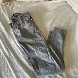 Replay Anbass grå slim jeans - Snygga grå jeans från Replay, modell Anbass med slim fit. Jeansen har klassisk femficksdesign, svarta kontrastsömmar och detaljerad bakficka. Perfekta för dig som gillar en stilren och modern look.