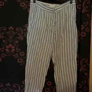 Randiga linnebyxor från H&M L.O.G.G. - Snygga och luftiga linnebyxor från H&M L.O.G.G. i vitt med blåa vertikala ränder. Byxorna har snörning i midjan och avslappnad passform, perfekta för varma dagar. Stl 42.