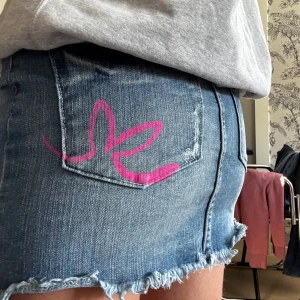 Playboy jeanskjol - Snygg vintage jeanskjol från Playboy med rå, fransig kant och rosa Playboy-logga på bakfickan. Klassisk femficksmodell med bälteshällor och rosa detaljer i sömmarna.