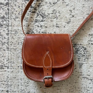 Vintage läderväska - 70-80-tal. Helt i läder. Hel och fint skick för sin ålder, dock lite fläckar. Ca 15x15x5 cm. Justerbar axelrem.