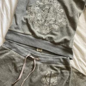 Vintage Juicy Couture sett  - Grått Juicy Couture sett i en äldre modell💕 Tyvärr för stort på mig💕Både koftan och byxorna är en XXL men de är mycket mindre i storleken, snarare en L💕 (Byxorna passar okej på mig som är en S) defekter: Byxorna är slitna i slutet av benen ( sista bilden) trycket på både tröjan och byxorna saknar stenar ( syns i bilderna)💕 Kan skicka fler bilder!