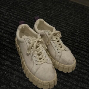 Etys  - Säljer ett par chunky vita sneakers med kraftig, räfflad sula och snörning. Skorna har en rund tå och är tillverkade i mocka-liknande material. Lila detaljer på hälen ger en cool kontrast. Perfekta för dig som gillar streetstyle och vill sticka ut.