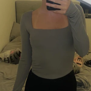 Grå långärmad topp med fyrkantig ringning - Snygg grå långärmad topp med en modern fyrkantig ringning. Toppens passform är tight och den är perfekt att styla med både jeans och kjol. Enkel och stilren design som passar till många olika looks.