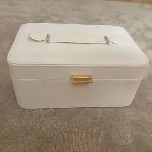 Vit smyckesväska med spegel - Stilren vit smyckesväska i syntet med guldiga detaljer och praktiskt handtag. Insidan har flera fack, ringrullar och en spegel i locket. Priset kan diskuteras vid snabb affär💗
