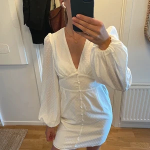 Vit kortklänning från NA-KD med puffärm - Superfin vit kortklänning från NA-KD. puffiga långärmar och dekorativa knappar framtill. 