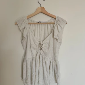 Vit blus  - Vit blus med volangärmar och knytning framtill. Blusen har en lätt rynkad struktur och v-ringning, vilket ger en luftig och somrig känsla.