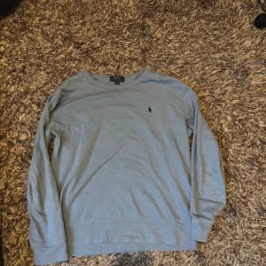 Ljusblå tröja från Polo Ralph Lauren - Snygg ljusblå långärmad tröja från Polo Ralph Lauren med klassisk broderad logga på bröstet. Tröjan är i mjuk bomull och har en enkel, clean design som passar perfekt till jeans eller chinos.