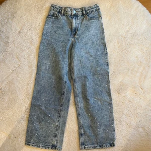 Blå jeans med pärldetaljer - Snygga blå jeans med raka ben och hög midja. Jeansen är dekorerade med små pärlor över hela framsidan för en extra cool touch.