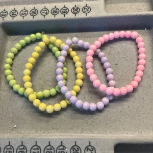 Pastellfärgade pärlarmband - Fyra elastiska armband med runda pärlor i pastellfärger: ljusgrön, gul, lila och rosa. Perfekta för att ge din outfit en söt och färgglad touch. Pärlorna är blanka och armbanden är stretchiga för enkel användning. De är handgjorda! 17kr st och 55kr för alla!