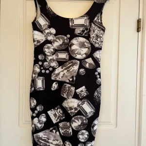 Svart klänning med diamantmönster Vero Moda - Cool svart kortklänning från Vero Moda med stora, glittriga diamantmönster i vitt och grått. Ärmlös och figurnära modell som verkligen sticker ut. Perfekt för dig som vill ha en unik look och älskar statement-plagg.