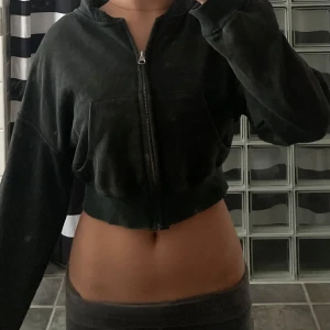 Svart croppad hoodiejacka med dragkedja - Svart croppad hoodiejacka med dragkedja framtill och stora fickor. Jackan har en loose passform och långa ärmar, perfekt för en chill och avslappnad stil. Mjuk och bekväm, passar till många outfits. Säljer pågrund av att den inte kommer till användning längre.